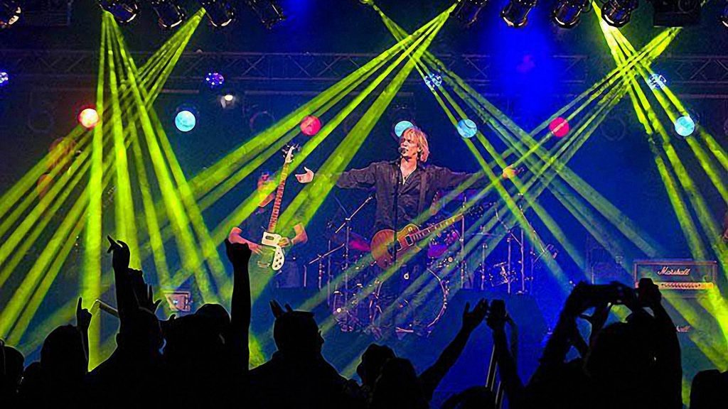 David Victor performing with a guitar on a concert stage under green and blue lights before a cheering crowd