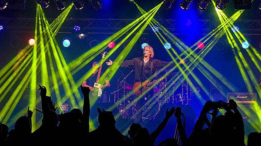 David Victor performing with a guitar on a concert stage under green and blue lights before a cheering crowd